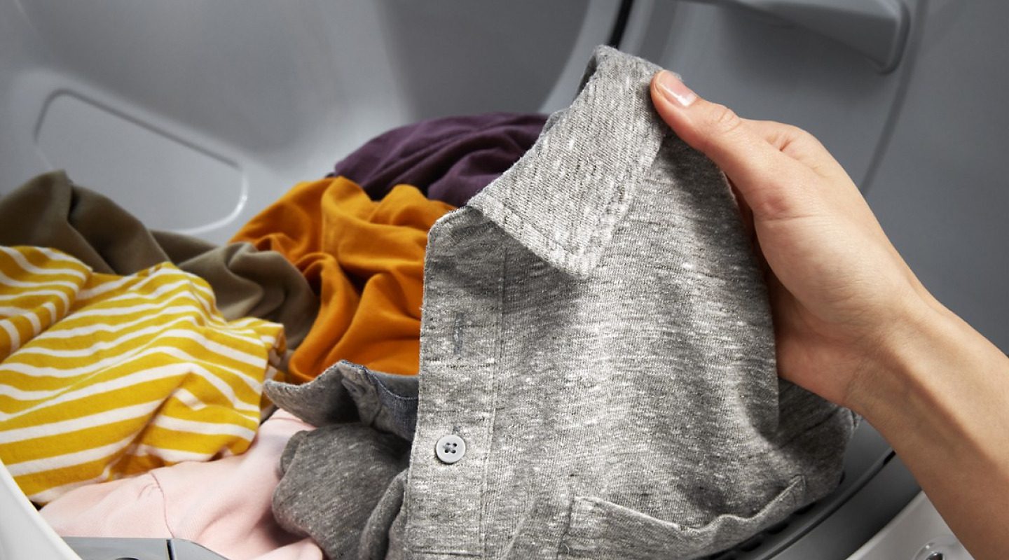 Một người lôi chiếc áo polo màu xám ra khỏi máy giặt. Một người lôi chiếc áo polo màu xám ra khỏi máy giặt.